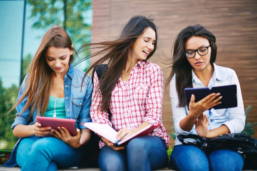 Three attractive young women sitting outside and reading together