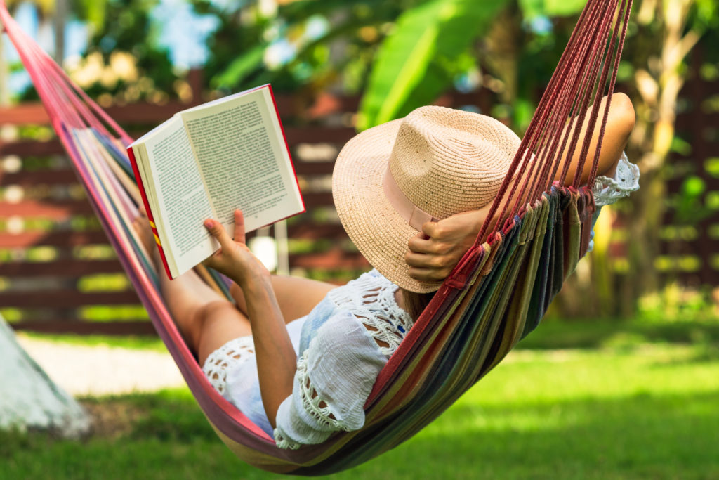Woman reading book in hammock outside on a sunny day