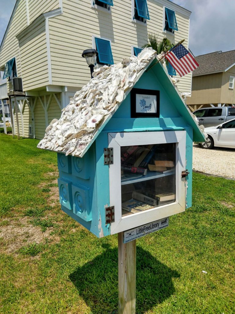 Little Free Library outside on lawn at Ocean Isle Beach North Carolina. Small American Flag flying from library's roof.