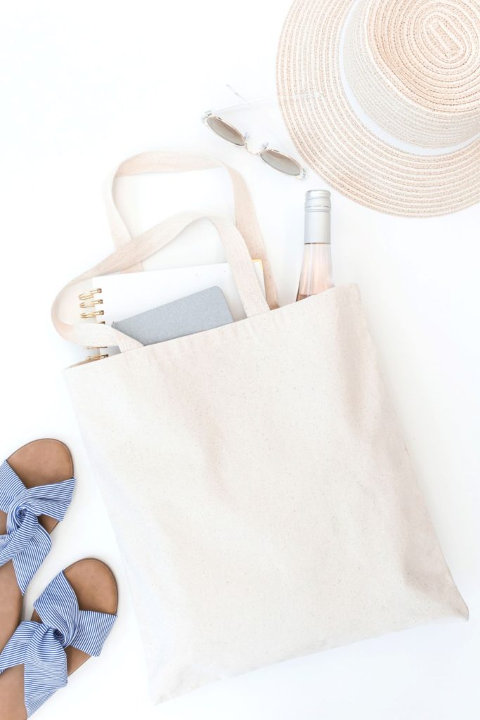 Blue sandals and white tote bag filled with water bottle, notebook and best summer books to read.